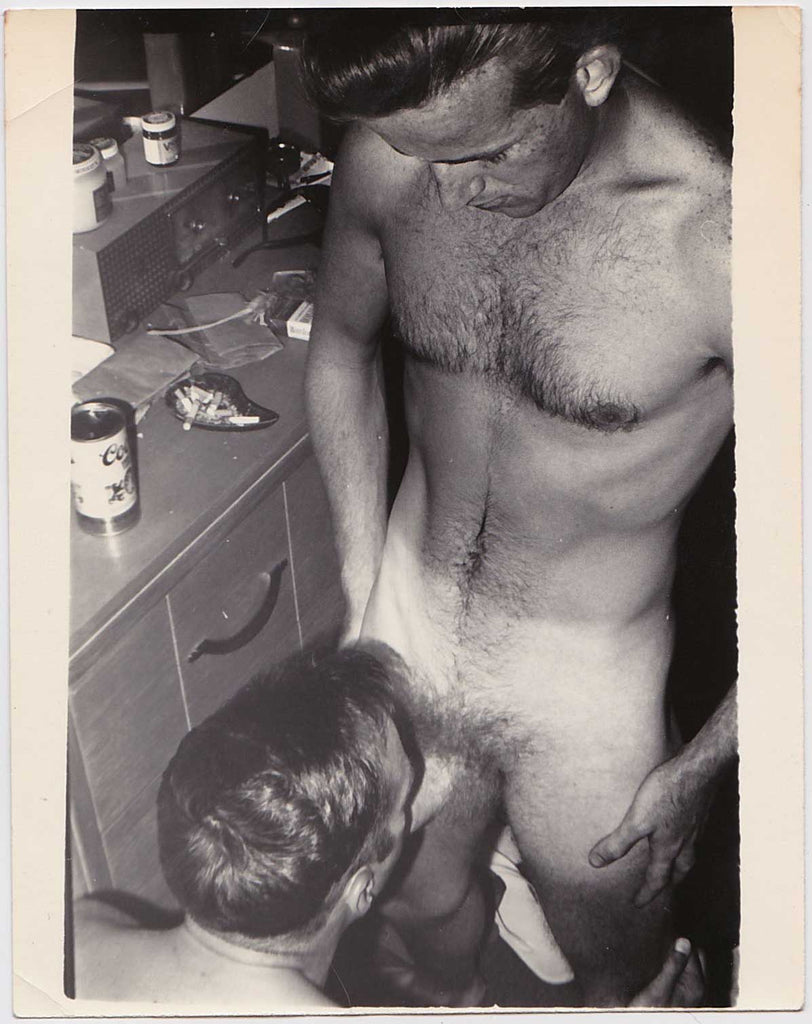 Handsome, hairy-chested guy on the receiving end as his partner kneels before him vintage gay photo.
