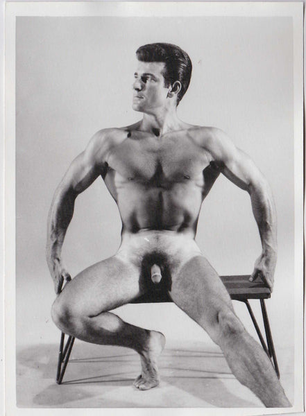 Vintage physique photo of handsome dark-haired Reno sitting on a low bench.