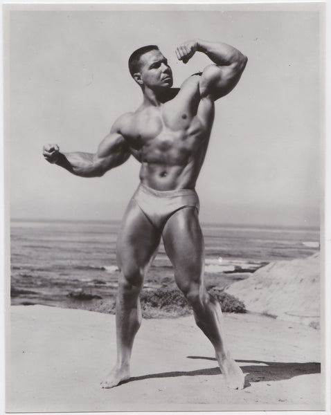 Bodybuilder Bill Pearl flexes on beach vintage photo