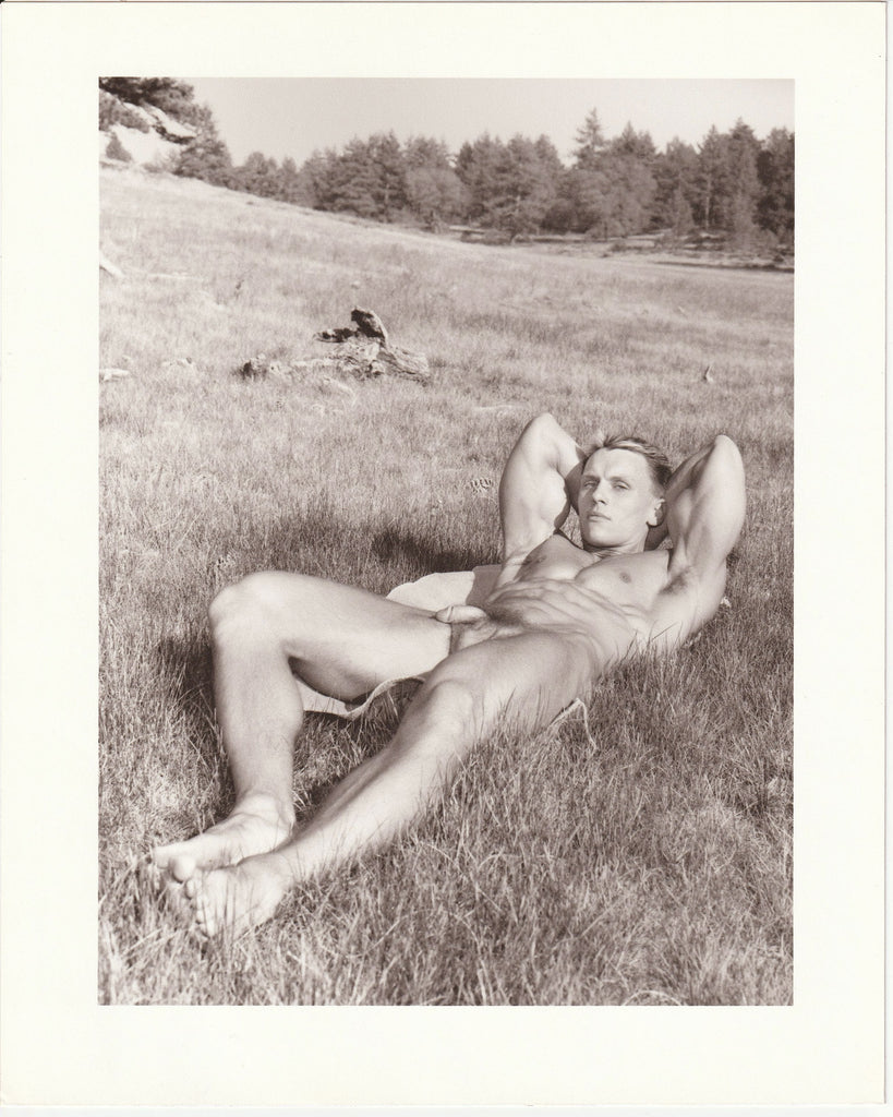 Beautifully printed photo of a handsome bodybuilder lying on the grass, revealing his biceps and abs. Signed and stamped on verso: "Paul Burkhart, San Diego, Calif." 