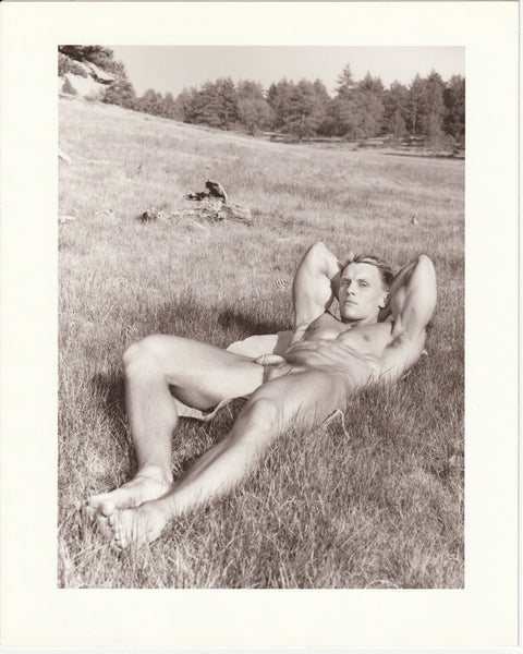 Beautifully printed photo of a handsome bodybuilder lying on the grass, revealing his biceps and abs. Signed and stamped on verso: "Paul Burkhart, San Diego, Calif." 