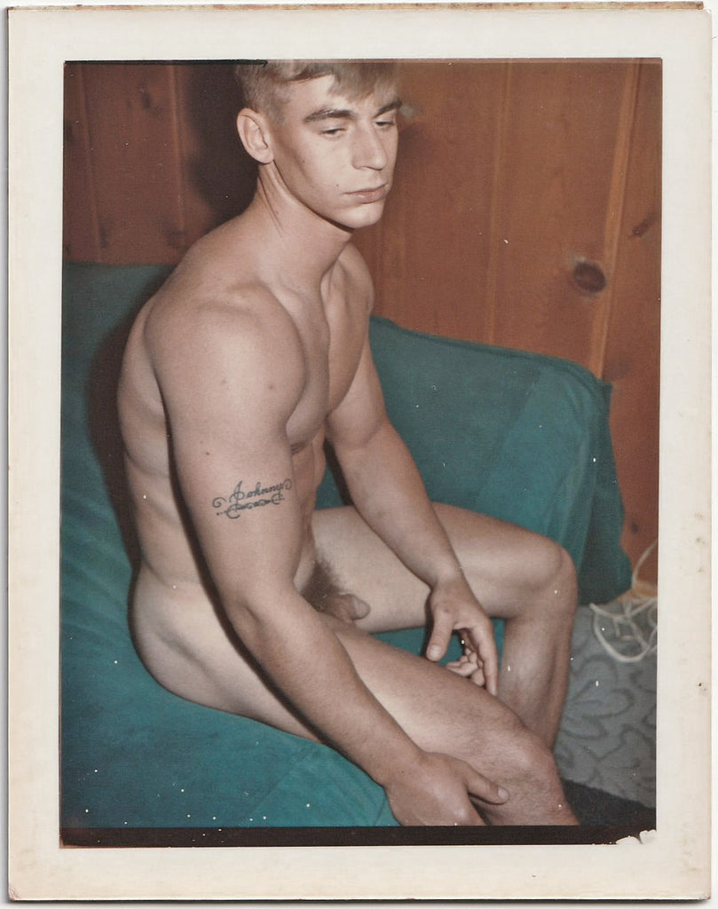 A vintage gay Polaroid of a male nude sitting on a bed.