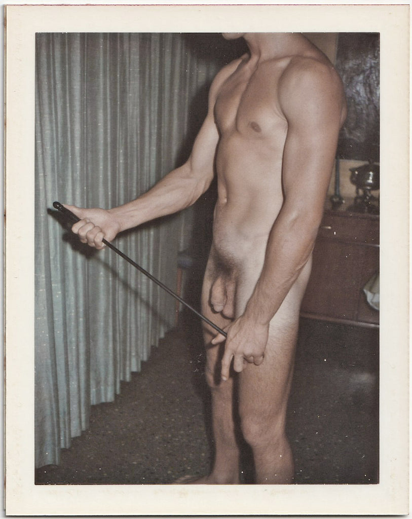 Male nude standing in the living room, holding a poker. 3 1/2" x 4 1/4" vintage gay Polaroid c. 1965.