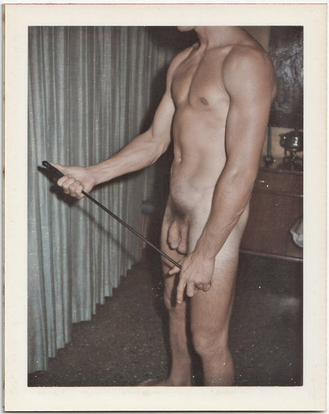 Male nude standing in the living room, holding a poker. 3 1/2" x 4 1/4" vintage gay Polaroid c. 1965.