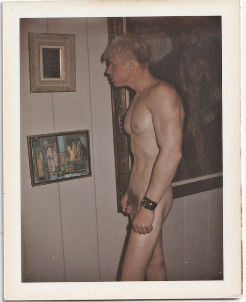 Vintage gay Polaroid nude muscular blond man examines a painting that's too dark to see in the photo.