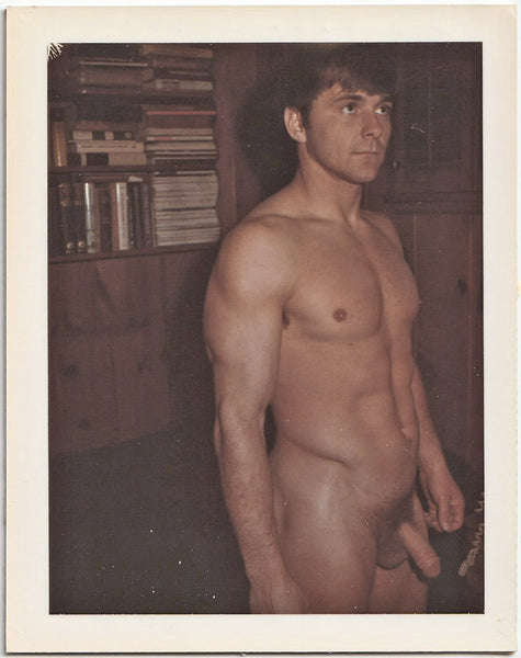 Vintage gay Polaroid male nude handsome muscle guy stands in the library with a faraway look in his eyes.
