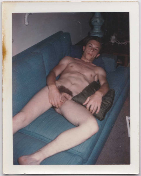 A muscular young guy reclines on blue sofa vintage gay Polaroid