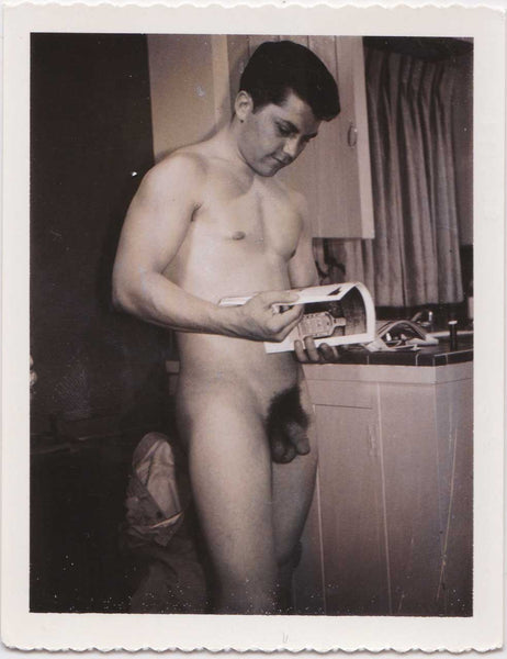 Vintage gay Polaroid Naked man standing in the kitchen, looking at a magazine. 