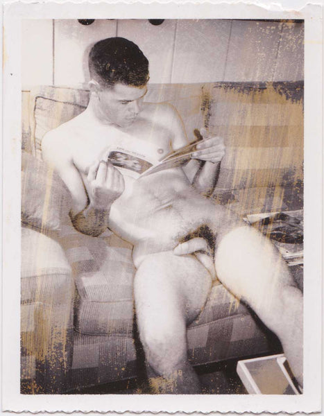 Vintage gay Polaroid Seated male nude looks at a magazine.