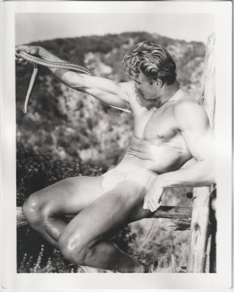 Ed Fury playing with a Gopher snake while sitting on a fence.  Vintage gay physique photo attributed to AMG.