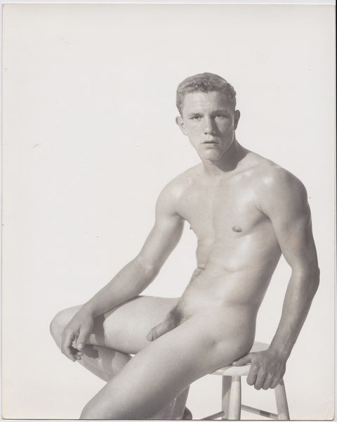Handsome young athlete seated on a wooden stool. Vintage male nude