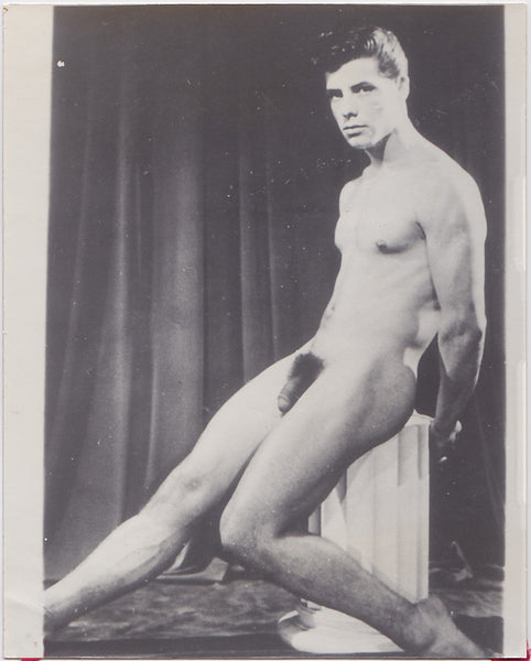 Handsome male nude with big legs sits on a column pedestal.  Vintage physique photo