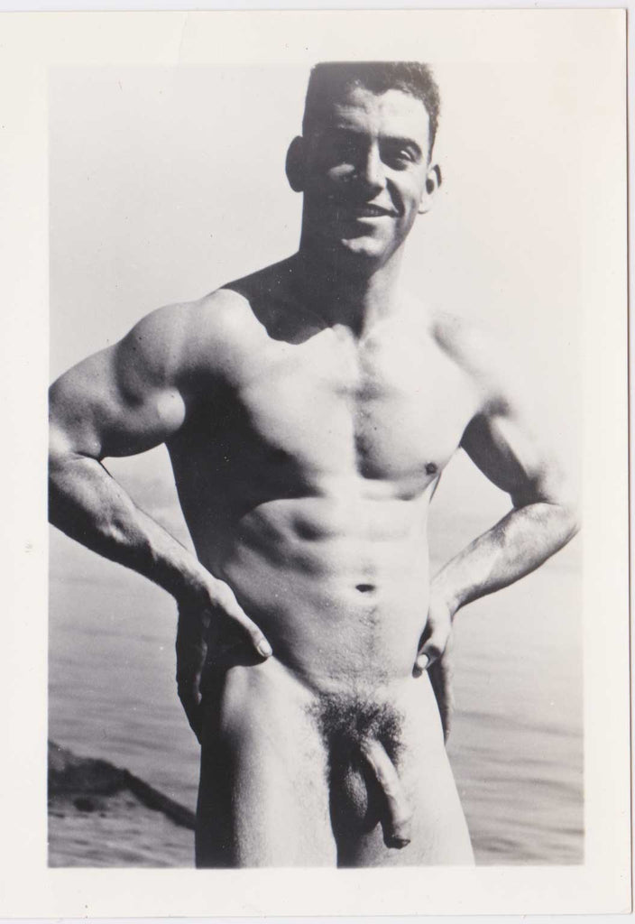 Handsome, hung and muscular guy stands on the beach with hands on hips vintage gay photo