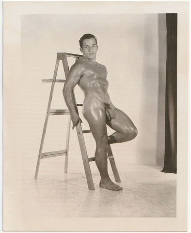 Shiny John Manning leans against a ladder in the studio vintage physique photo.