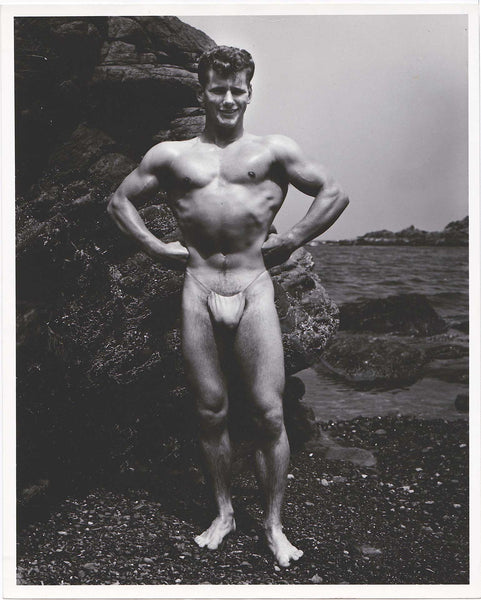 Original photo of a handsome male model (Joe Survilas) standing on a rocky beach with arms akimbo.