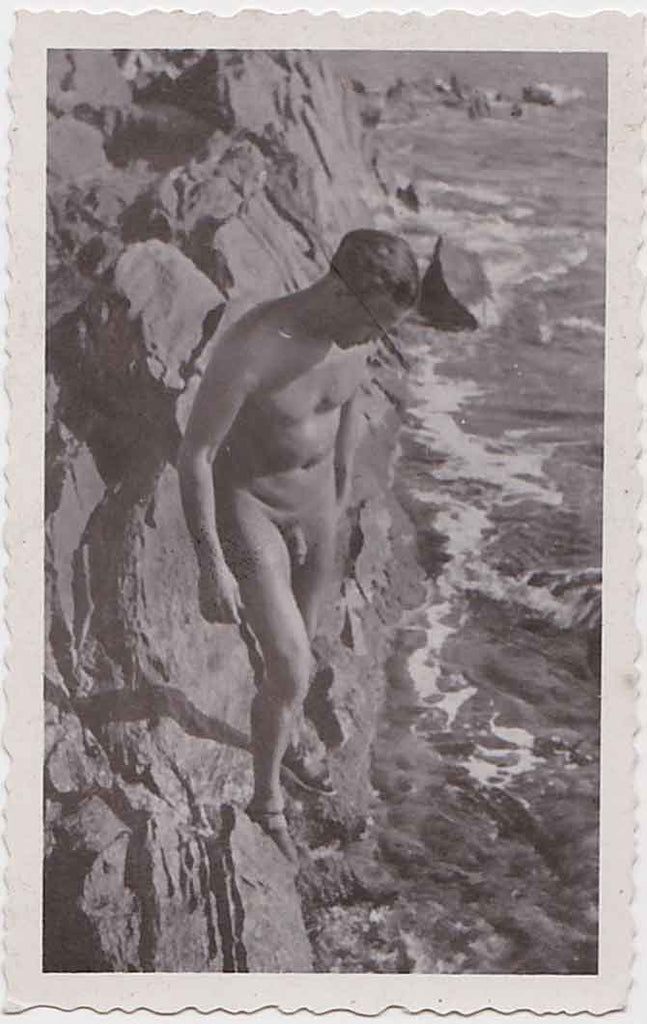 Beautifully composed and quietly elegant male nude standing on rocks, gazing down at the water.