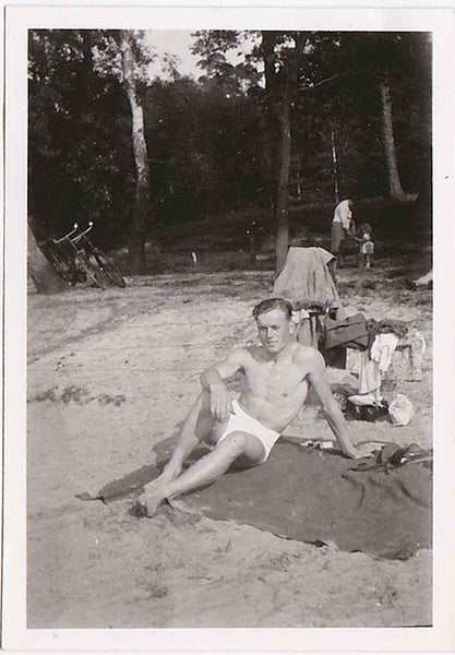 Handsome guy in white swim trunks reclines on a blanket. vintage gay snapshot