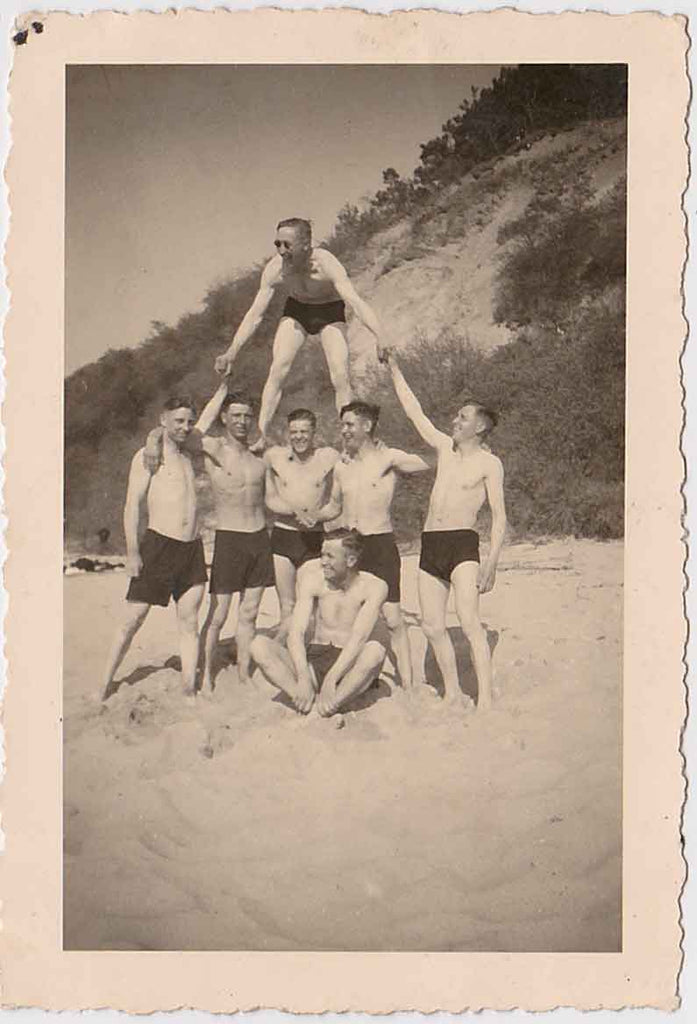 Vintage black and white photo of a pyramid formation on a beach with men in swimsuits.