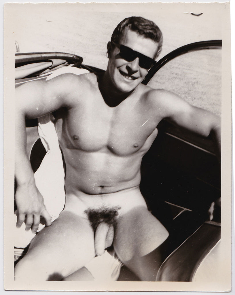 Young Helmut Reidmeier wearing shades as he sits naked in the back seat of a car vintage gay photo.