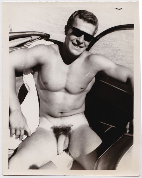 Young Helmut Reidmeier wearing shades as he sits naked in the back seat of a car vintage gay photo.