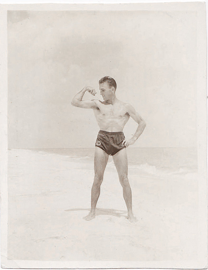 Vintage sepia photo Handsome guy (lifeguard?) flexes his biceps on the beach.