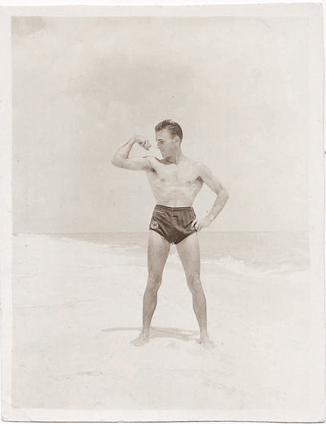 Vintage sepia photo Handsome guy (lifeguard?) flexes his biceps on the beach.