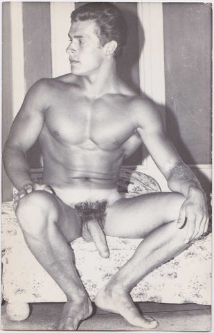 Original vintage photo of well-endowed, muscular, handsome young Helmut Riedmeier seated on a bed.