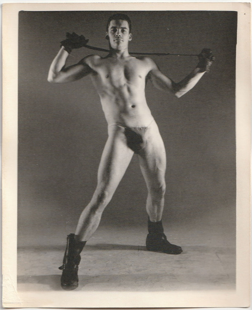 Vintage physique photo by Kris Studios of a man in a posing strap holding a whip.