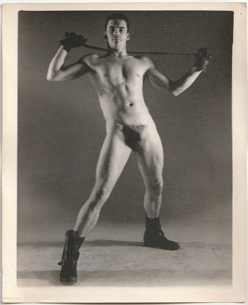 Vintage physique photo by Kris Studios of a man in a posing strap holding a whip.