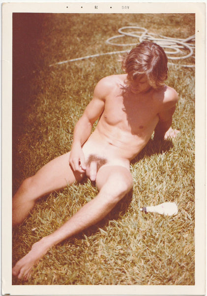 Sexy guy reclines on the grass with a bottle of either sunscreen or lube.