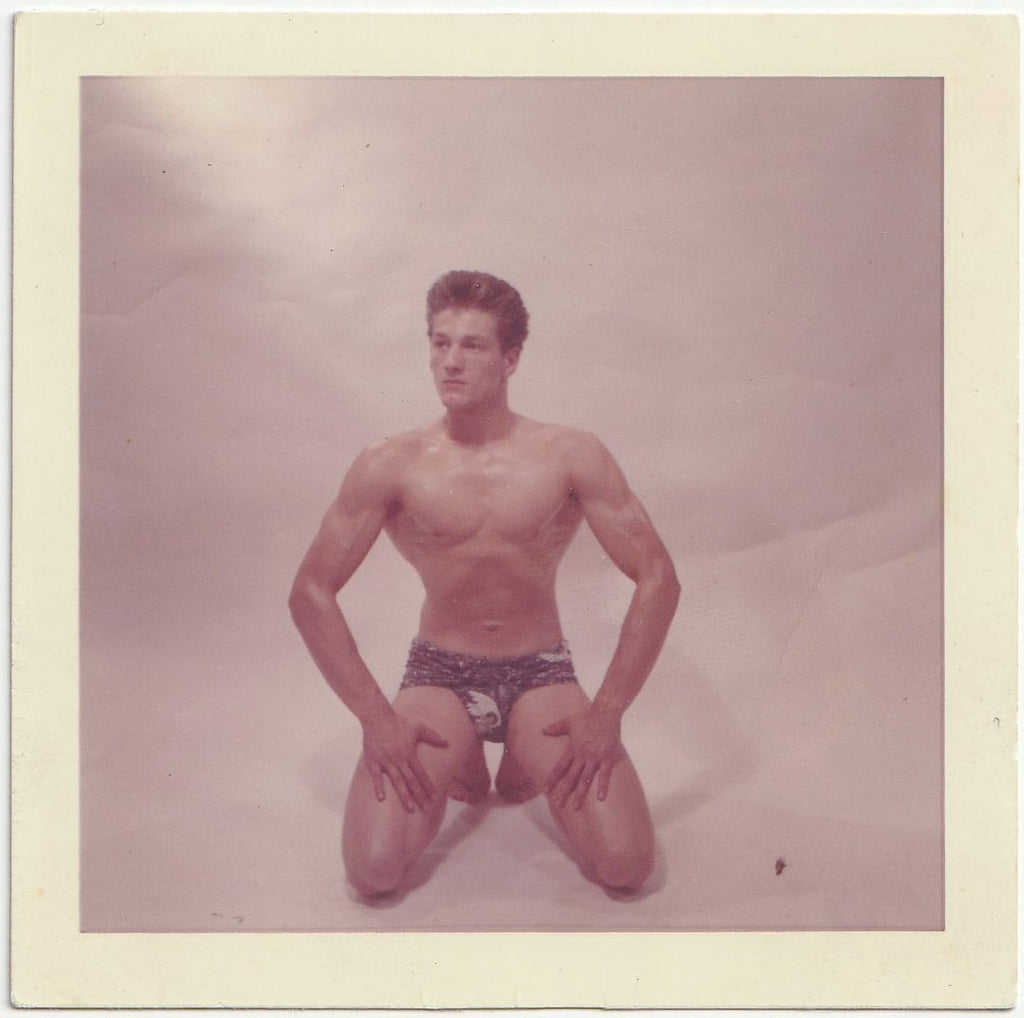 Handsome broad-shouldered guy kneels in a studio vintage gay physique photo.