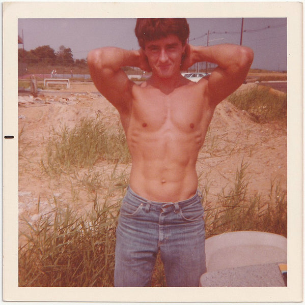 Sexy guy stands in a field showing off his upper body development. Vintage gay color snapshot