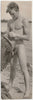 A vintage black and white photograph depicting a nude young man standing on a beach while holding a wet towel.