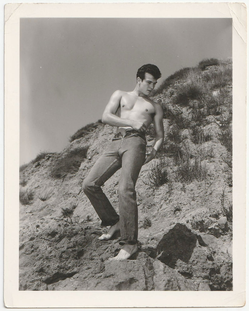 Handsome shirtless guy with very tight jeans stands shirtless and shoeless on a mountainside vintage gay photo.