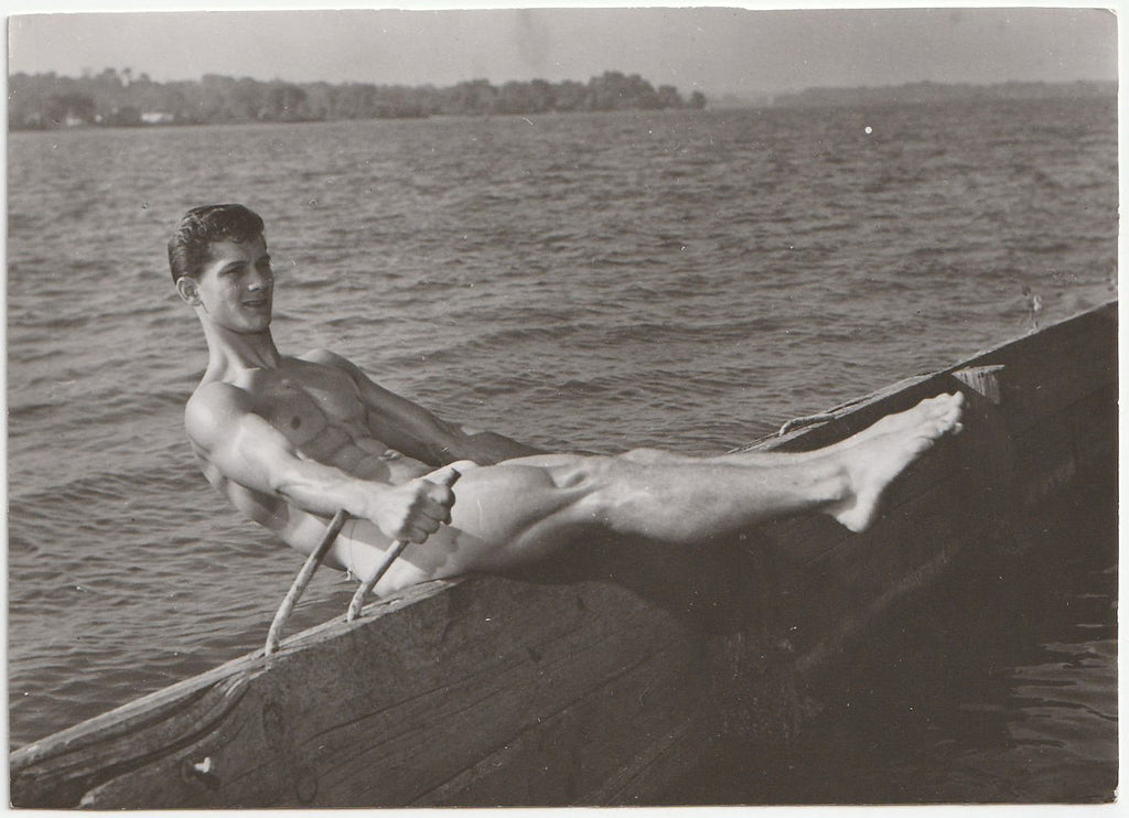 Black and white vintage gay photograph of a bodybuilder doing a sit-up on a pier.