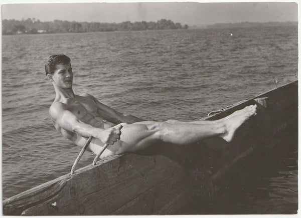 Black and white vintage gay photograph of a bodybuilder doing a sit-up on a pier.