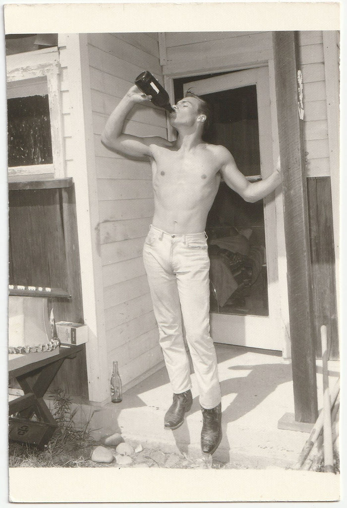 Handsome shirtless guy standing on the front stoop drinking from a big bottle vintage gay photo