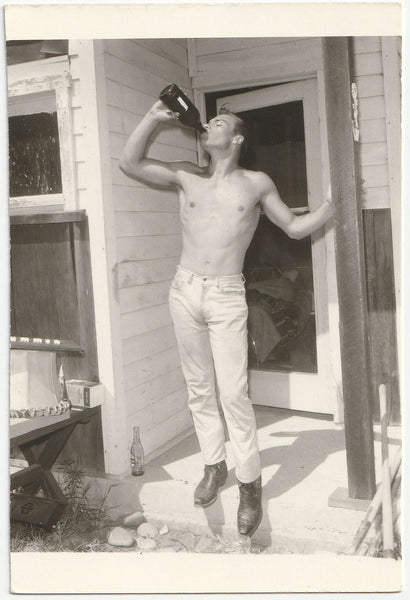 Handsome shirtless guy standing on the front stoop drinking from a big bottle vintage gay photo