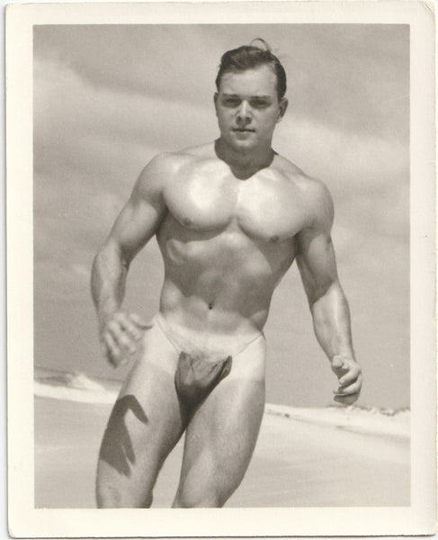Cute muscle guy with nice tan lines jogs on an empty beach wearing only his posing strap. Vintage physique photo.