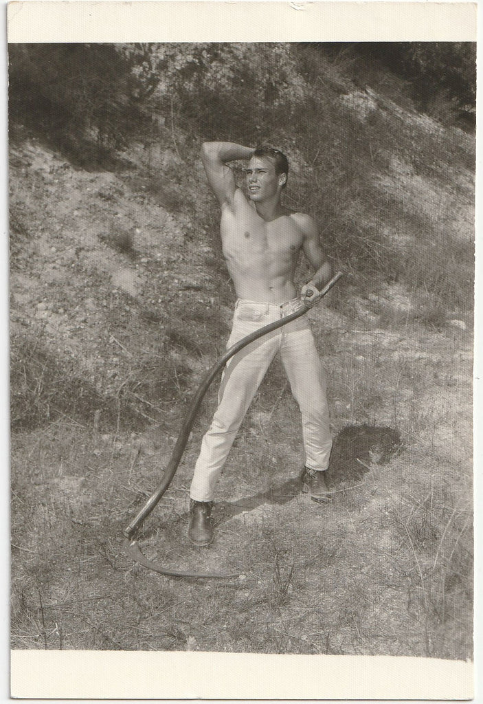 Handsome shirtless guy shows off his muscular physique while holding what appears to be a curved scythe.