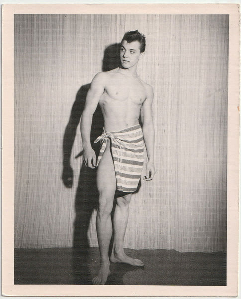 Vintage physique photo Dark-haired guy gives a sideways glance while posing in a carefully knotted towel. For what it's worth, he has very big feet.