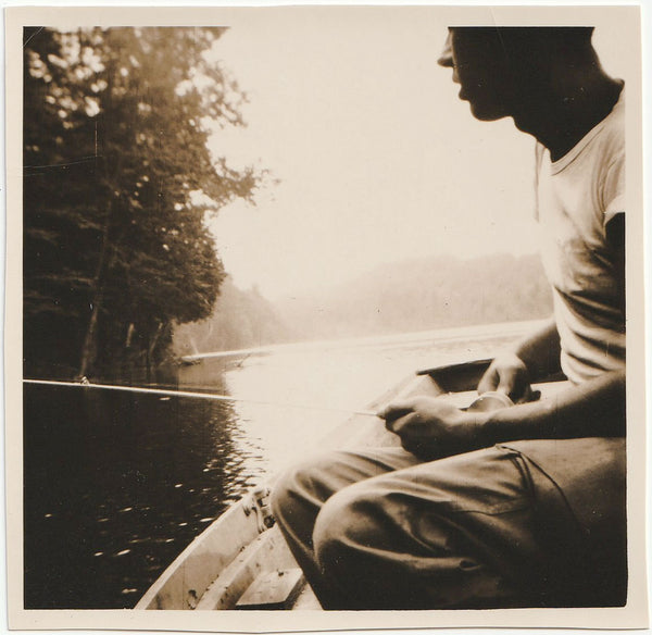 Artfully composed image of a man in profile, sitting in a rowboat with a fishing line.