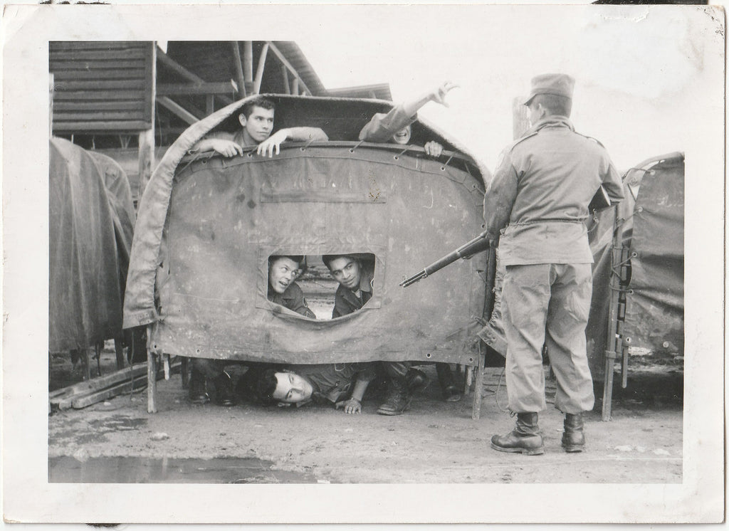 Husky guard identified on verso as "Manriges (Calif)" stands watch over five GIs in a not-very-secure tent.