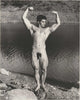 Original vintage photo of handsome Oakland weightlifter and cyclist Doyle Brewer flexing beside a river.