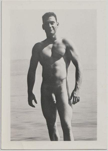 Handsome hunk stands with confidence against an ocean backdrop. Vintage male nude photo.