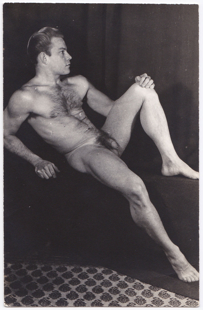 Handsome hairy-chested male nude reclining on plinth displays his muscular physique.