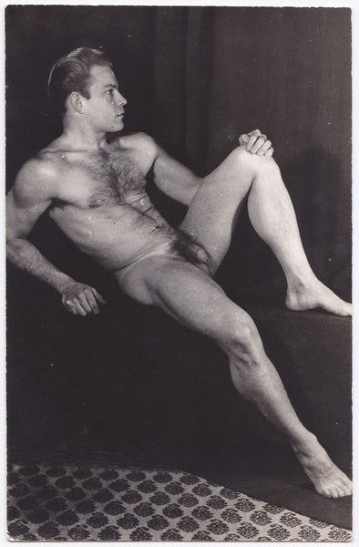 Handsome hairy-chested male nude reclining on plinth displays his muscular physique.