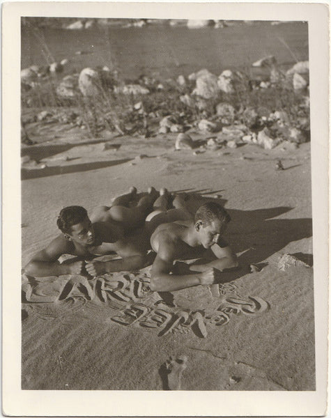 Vintage gay photo Two naked guys lying on their bellies, writing names in the sand. 