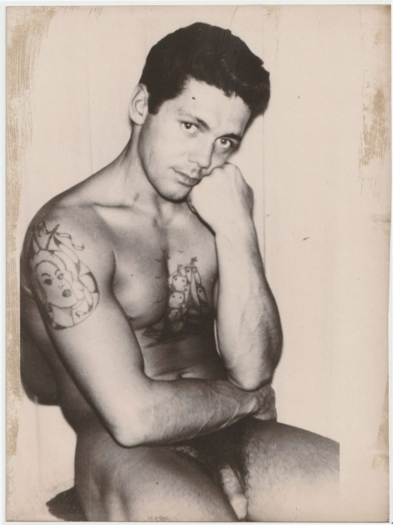 Large format vintage gay photo of an unidentified seated male nude one might presume to be a sailor with a rather penetrating gaze.