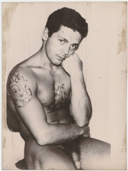 Large format vintage gay photo of an unidentified seated male nude one might presume to be a sailor with a rather penetrating gaze.